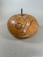 Photo showing side view of round hollow gourd with carved floral and abstract designs, featuring perforations and a short stem on top.