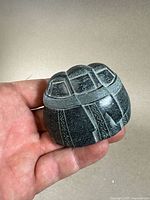 Photo showing three Inuit figures carved in black soapstone with detailed etched faces and clothing, held in hand for scale.