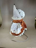 Side view of the handmade chef mouse doll showing brown floral dress, white apron and grey chef hat with bead tips.