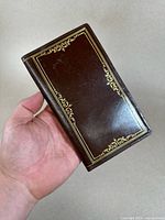 Photo showing the closed wallet exterior with gold decorative trim held in hand, highlighting the handmade leather and design details.