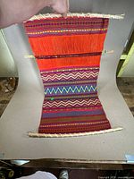 Top view of decorative hanging loom with colorful woven textile, showing red and purple yarns and wooden frame sticks