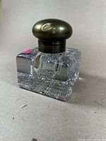 Side view of the huge antique inkwell showing the clear, thick crystal square base and round brass lid with dents.