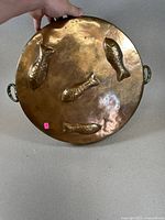 Top view of large round copper pan with four embossed fish shapes on bottom surface.