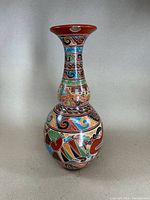 Front view of the large carved pottery vase showing colorful geometric and abstract carved and painted patterns on the bulbous body and neck, red clay base.