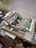 Fishing tackle box opened showing large lead sinkers and assorted fishing accessories inside compartments and trays.