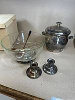 Photo showing large clear glass salad bowl with a metal spoon inside, silver plated ice bucket with lid and handles, and two small silver plated candlestick holders.