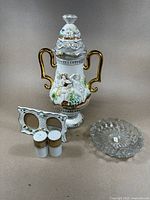 Porcelain ewer with gold handles, double picture frame, salt and pepper shakers, and crystal bowl arranged on a flat surface