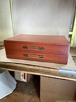 Front view of the mid-century modern walnut storage case with two drawers closed, showing metal handles and keyholes.