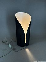 Front view of the black and white curved pedestal light illuminated, showing design and light effect.