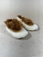 Side and angled view of the antique children's moccasins showing white fur base with brown fur around ankle area.