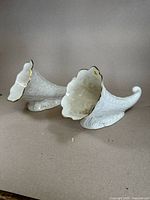 Side view showing two white porcelain cornucopias with detailed fruit and leaf embossing and curled tails