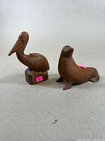 Two carved wooden animals, a pelican and sea lion, made in walnut wood with natural finish and folk art styling.