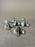 Set of seven small silver fortune cookie-shaped photo holders on a surface, showing all items together.
