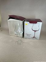 Photo showing two boxes and one clear wine glass from the set, the glasses are part of the Signature Series by JG Durand in the Le Bordeaux style.