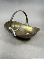 Angled view of kidney-shaped silver plated brass log holder highlighting its smooth finish, handle with groove detail, and internal brackets.