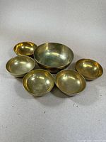 Group photo showing six Chinese brass singing bowls, five smaller with dragons and one larger plain