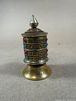 Front view of brass prayer scroll holder with ornate Tibetan script and colored stones