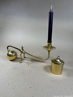 Full view of brass candle holder with black taper candle placed in holder, showcasing the weighted ball counterbalance on one end and candle cup with drip tray on the other end.