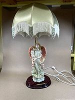 Full view of angel statue lamp with cream fabric shade and fringe