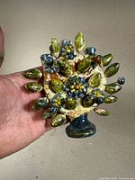 Close-up of ceramic Tree of Life sculpture showing detailed leaves, fruits, and floral motifs with green, yellow, blue, and brown glaze.