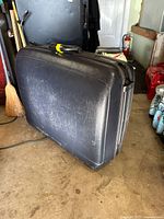 Side view of vintage black hard shell Samsonite suitcase showing scuffs and scratches on textured exterior and a luggage handle.