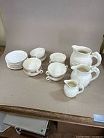 Full set of white embossed porcelain items including soup terrines, pitchers, plates, and bowls arranged on table.