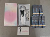Facial skin care massager in tray with USB cable beside boxed serums and product box