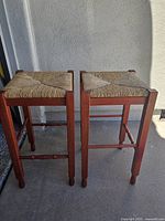 front view of both red wood bar stools with woven seats