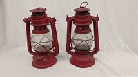 Two red hurricane lanterns side by side, full view