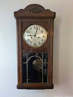 Full view of wall clock hanging with case, dial and glass showing pendulum