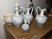 Group of four blue-and-white ceramic pitchers and one warming stand displayed on shelf
