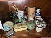 Shelf view showing assorted collectibles including desk calendar, trinket boxes, ginger jars, mugs, doll