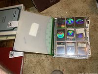 Open binder showing holographic alphabet cards in sleeves, binder cover visible