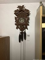 Full view of wooden cuckoo clock hanging on wall with three weights