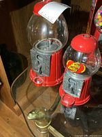 Both gumball machines side by side on glass shelf