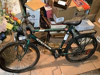 Full view of green CCM mountain bike with rear rack and kickstand surrounded by boxes