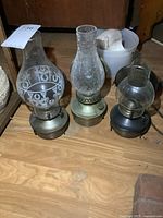 Three metal oil lamps side by side showing finishes and chimneys