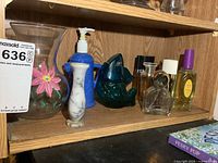 Wide view of entire bottom shelf showing vases, dispenser, fish pitcher, perfume bottles and book