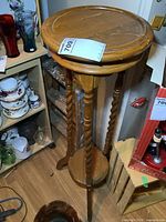 Full view of wooden plant stand showing round top, three spiral legs, lower shelf and feet