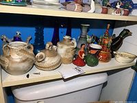Full shelf view showing pottery jugs, glass vases, ceramic pieces and wooden figures