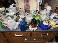 Overview of entire group of teapots and enamel pot on counter