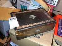 Closed writing box sitting on cardboard boxes, showing full form and size tag