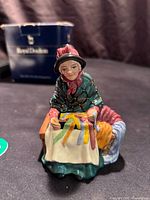Front view of Royal Doulton Street Vendors Silks & Ribbons figurine with box in background