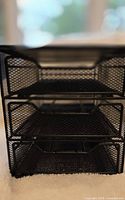 Front view of black metal mesh organizer showing three trays
