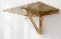 Table mounted on wall in open position showing birch top and support arm