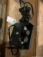 Photo of two black Tasco Zip 306Z binoculars, one inside a black carrying case with strap on marble surface.