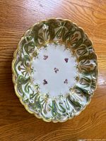 Top view of the antique Nippon porcelain plate showing the hand painted pink floral design in the center and the scalloped gilded edge with green and gold geometric patterns.