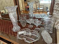 Full view of all 10 pieces including vases, compotes, trays, and jars arranged on table in front of mirror to show variety and detail.