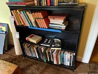 Photo showing the front of the black wooden bookcase filled with various books to illustrate shelves and size.