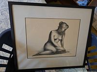 Full view of the framed artwork showing the seated nude female figure in black and white with visible frame and matting.